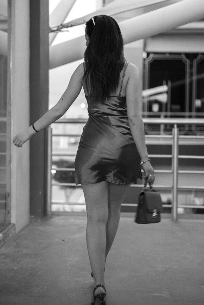 Black and white photo of a woman in a dress walking indoors, showcasing fashion and elegance.