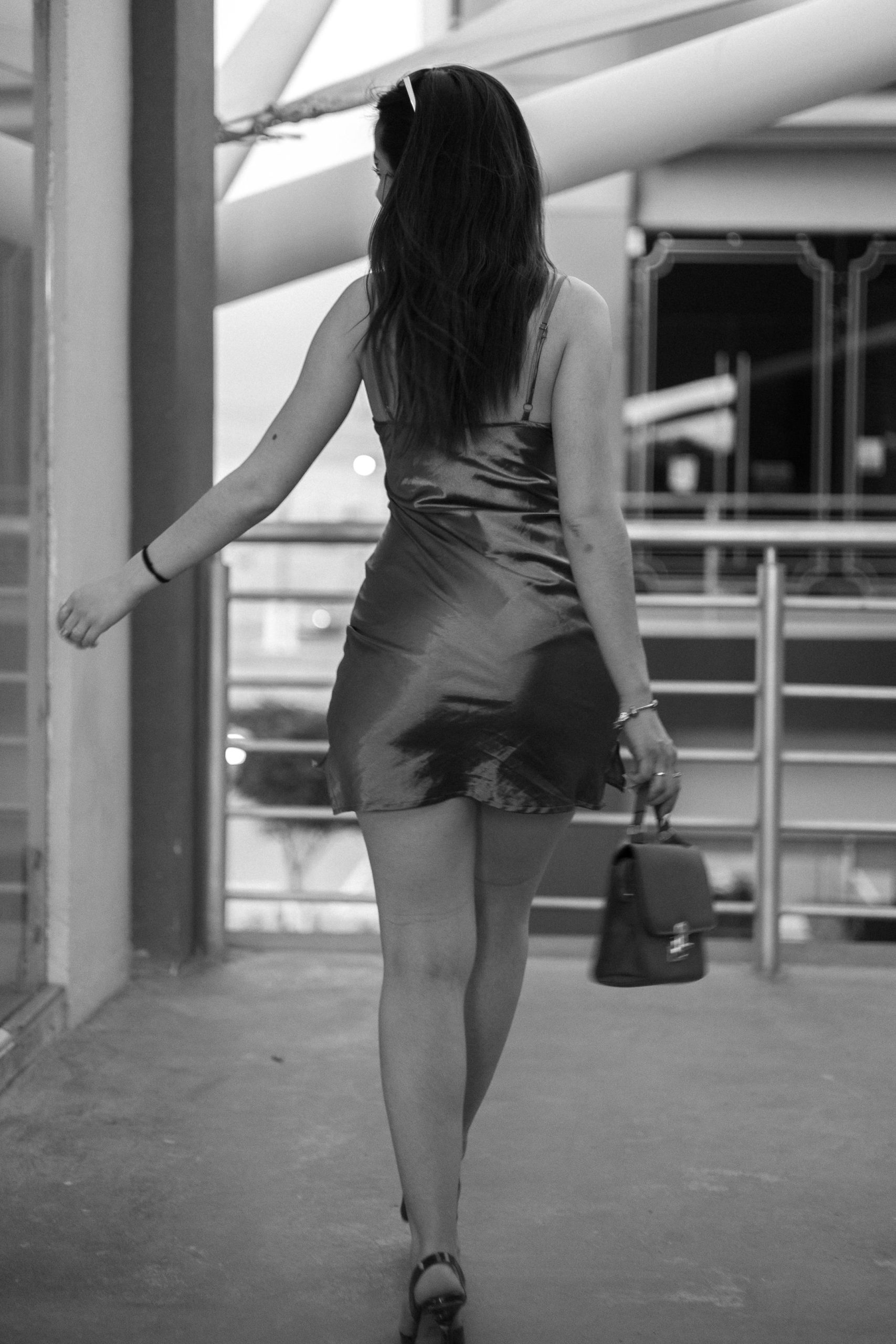 Black and white photo of a woman in a dress walking indoors, showcasing fashion and elegance.