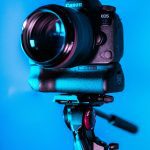Close-up of a DSLR camera on a tripod with a blue background.