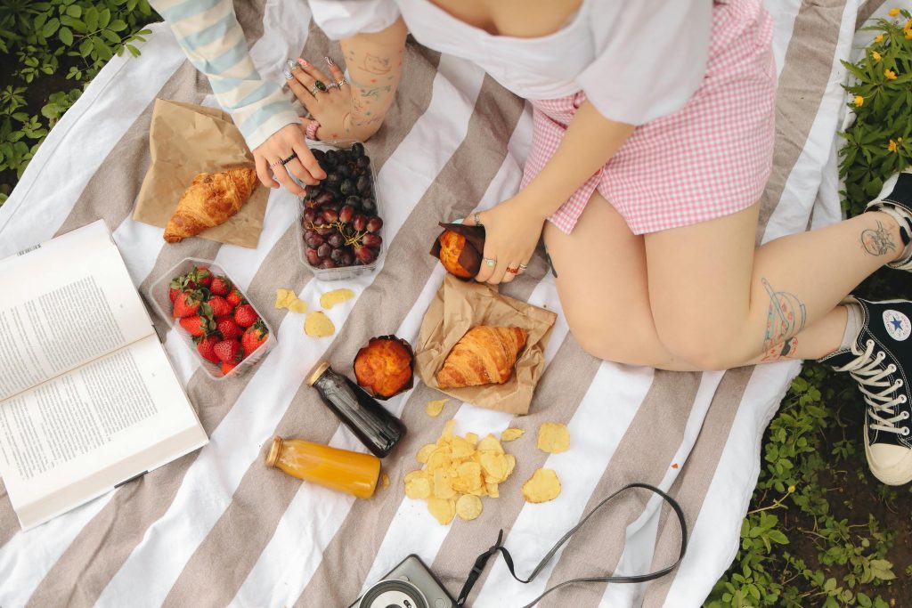 Overhead view of a vibrant picnic scene with fruits, pastries, and a book on a striped blanket.
